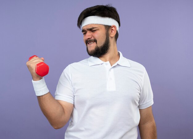 Jovem tenso e esportivo usando bandana e pulseira, fazendo exercícios com halteres