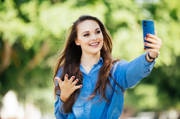 Jovem tira selfie de mãos com telefone na rua da cidade de verão. Conceito de vida urbana.