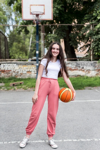 Jovem tiro grande, segurando uma bola de basquete fora