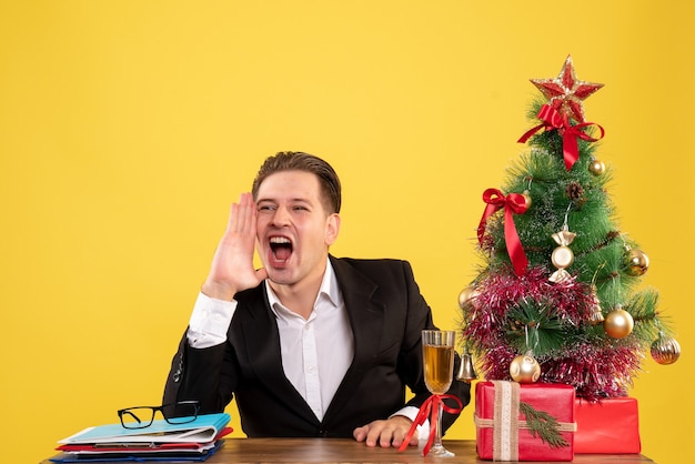 Jovem trabalhador do sexo masculino sentado com presentes de Natal e chamando a árvore