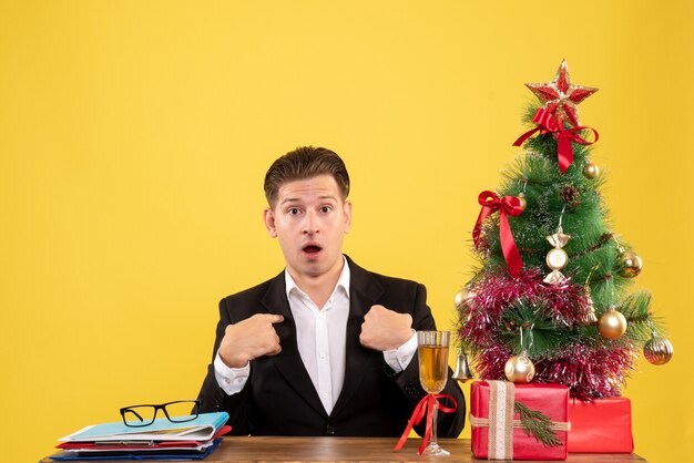 Jovem trabalhador do sexo masculino sentado com uma árvore e presentes de Natal