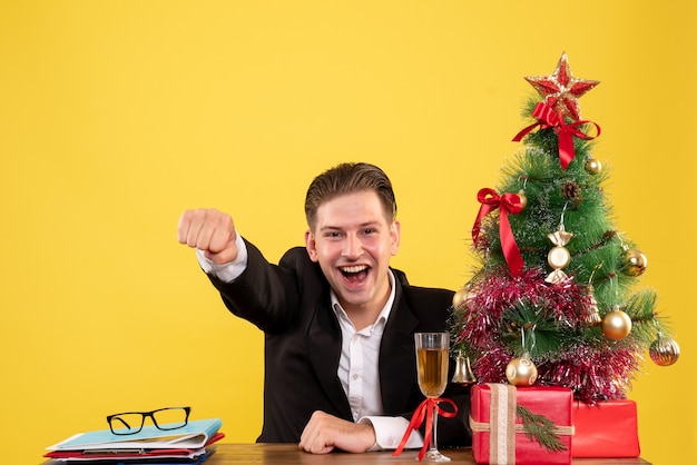 Jovem trabalhador do sexo masculino sentado de frente com os presentes de Natal e a alegria da árvore