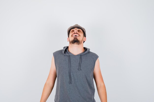 Jovem trabalhador em pé e posando na frente com uma camiseta cinza e boné e parecendo feliz