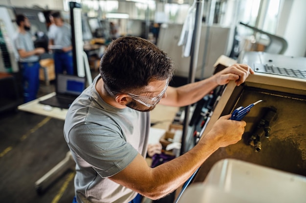 Jovem trabalhador manual trabalhando na máquina industrial em uma fábrica