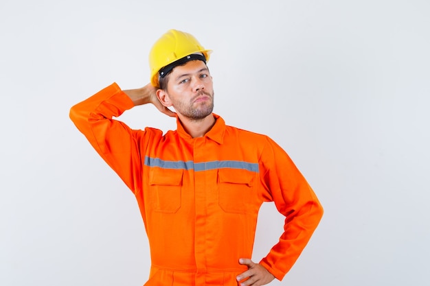 Foto grátis jovem trabalhador posando com a mão atrás da cabeça de uniforme, capacete e elegante.