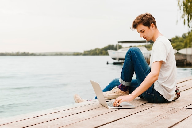 Jovem trabalhando no laptop à beira do lago