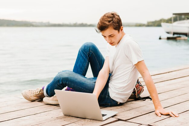 Jovem trabalhando no laptop à beira do lago