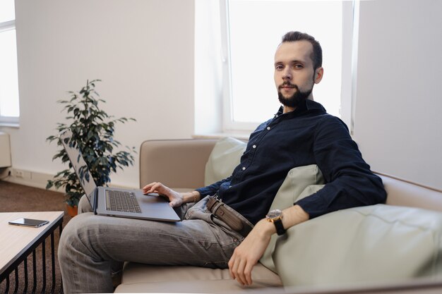 Jovem trabalhando no laptop enquanto está sentado no sofá no escritório