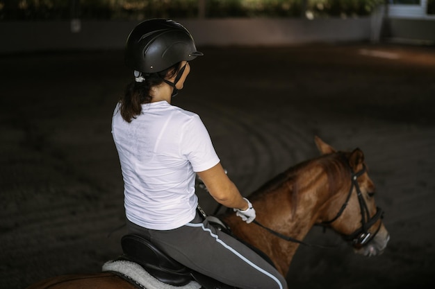 Jovem treina em passeios a cavalo na arena. jovem mulher caucasiana em roupas formais cavalgadas pela arena arenosa. um cavalo de pedigree para o esporte equestre. a desportista em um cavalo