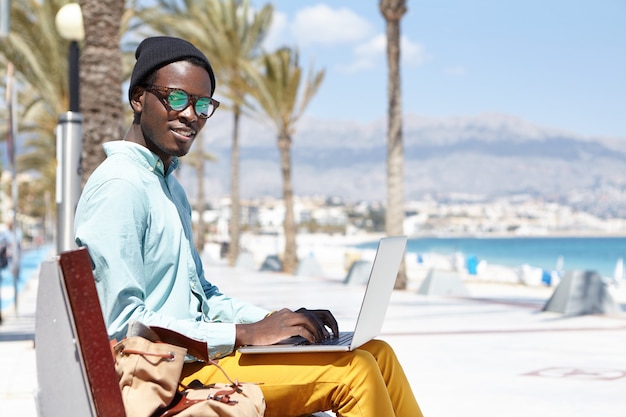 Jovem turista do sexo masculino sentado no banco com o laptop