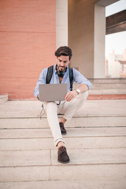 Jovem turista masculina sentado na escadaria usando laptop