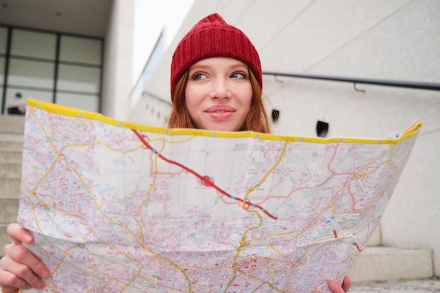 Foto grátis jovem turista ruiva sorridente senta-se na escada ao ar livre com mapa de papel da cidade procurando direção