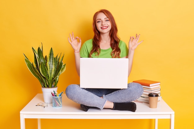 Jovem usando laptop para seu trabalho freelance, sentada na mesa branca, parece concentrada