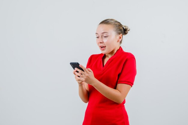 Jovem usando o celular em uma camiseta vermelha e parecendo feliz