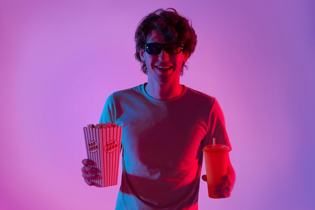 Jovem usando óculos 3d gostando de comer pipoca e assistir filme em fundo de luzes neon