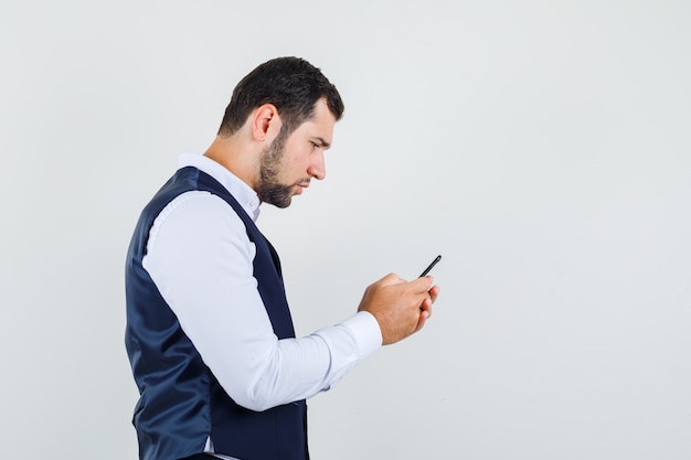 Jovem usando telefone celular com camisa e colete e parecendo ocupado.