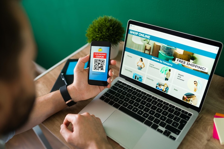 Foto grátis jovem usando um cupom de desconto em seu smartphone para fazer algumas compras online no laptop