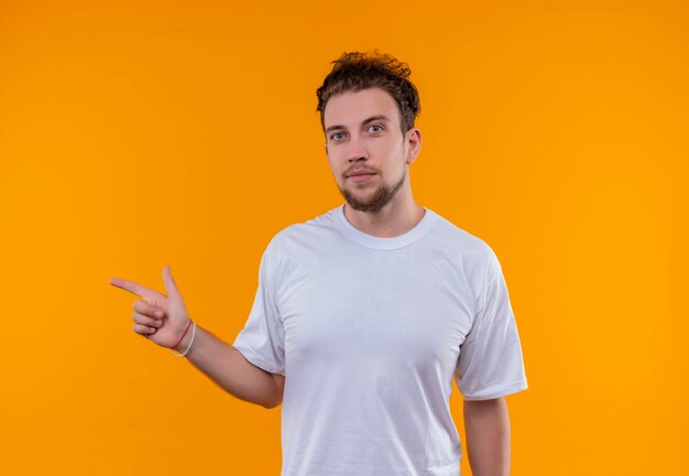 jovem vestindo camiseta branca apontando para o lado em uma parede laranja isolada
