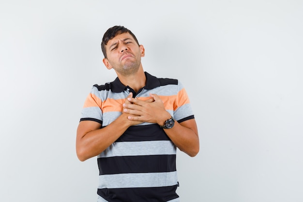 Jovem vestindo camiseta de mãos dadas no peito e parecendo dolorido