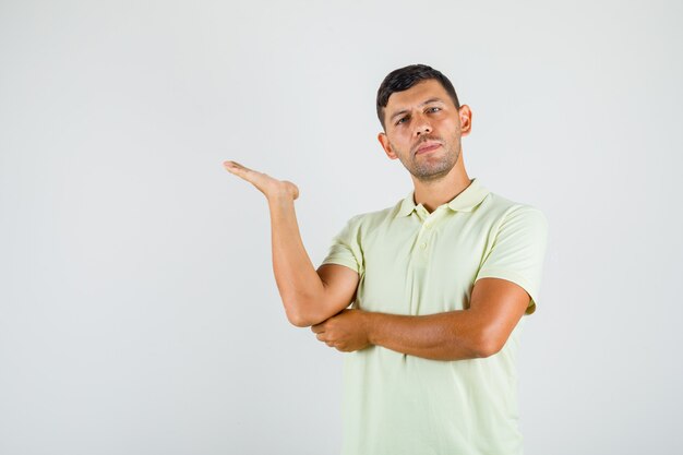 Jovem vestindo uma camiseta apresentando e apontando com a palma da mão aberta e parecendo confiante