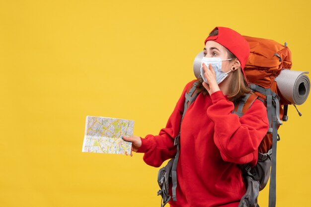 Jovem viajante com mochila e máscara segurando o mapa de viagem de frente