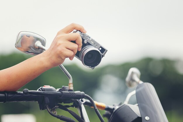 Jovem viajante masculino asiático e fotógrafo sentado na moto de estilo clássico, segurando a câmera