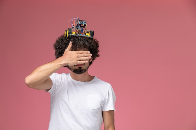 Foto grátis jovem, vista frontal, cobrindo os olhos com a mão e colocando seu robô eletrônico na cabeça