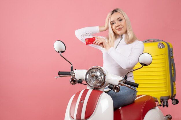 Jovem, vista frontal, em ciclomotor segurando um cartão e colocando a mão na cabeça