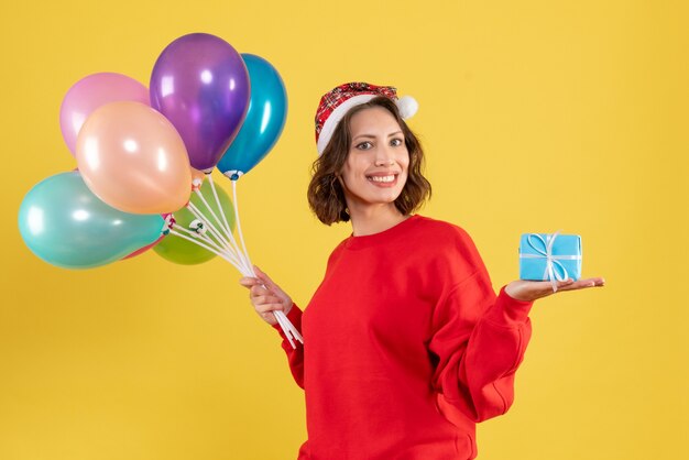 Jovem, vista frontal, segurando balões e um presentinho amarelo, feriado de natal, ano novo, cor, mulher, emoção