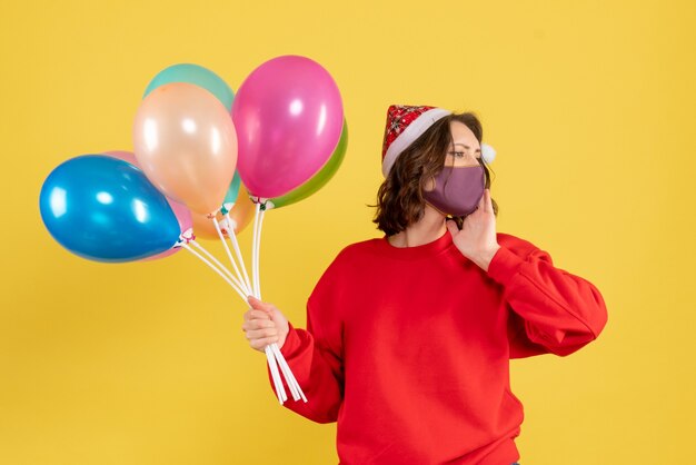 Jovem, vista frontal, segurando balões na máscara amarela