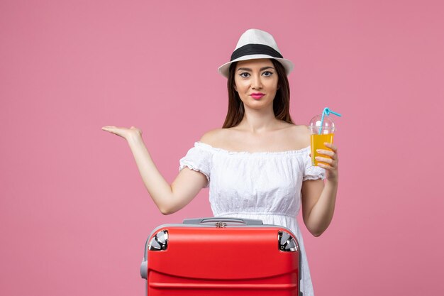 Jovem, vista frontal, segurando um coquetel com uma sacola de férias vermelha na parede rosa emoções férias avião viagem verão viagem