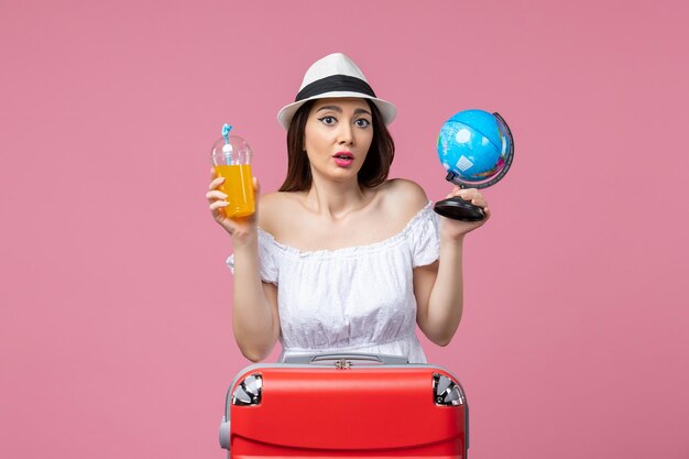 Jovem, vista frontal, segurando um globo e um coquetel na parede rosa verão viagem viagem calor cores férias