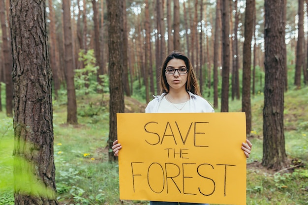 Jovem voluntária nos piquetes da floresta segurando um pôster salve a floresta