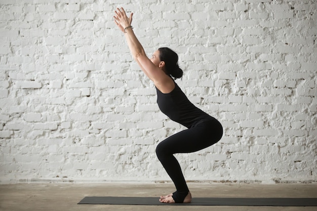 Foto grátis jovem yogi mulher atraente em utkatasana pose, loft backg branco