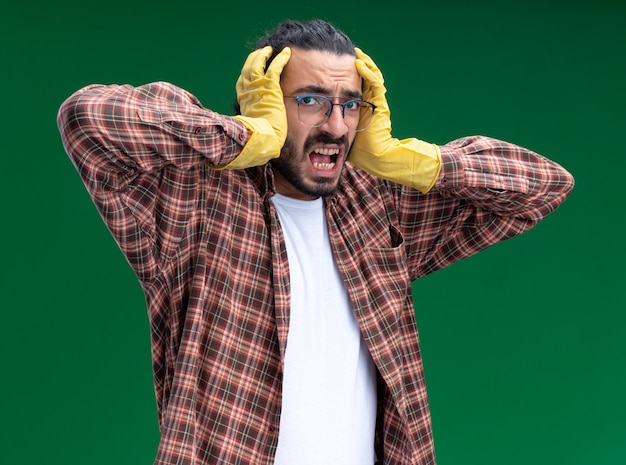 Foto grátis jovem, zangado, bonito, faxineiro, usando camiseta e luvas, agarrou a cabeça isolada na parede verde