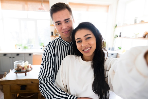 Jovens amantes abraçando e tomando selfie na cozinha