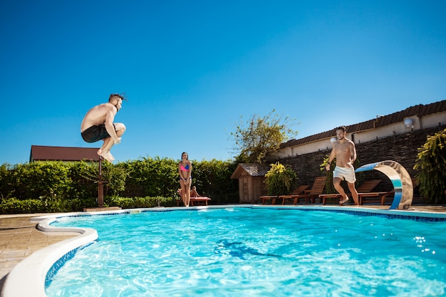 Jovens amigos alegres sorrindo, relaxando, pulando na piscina