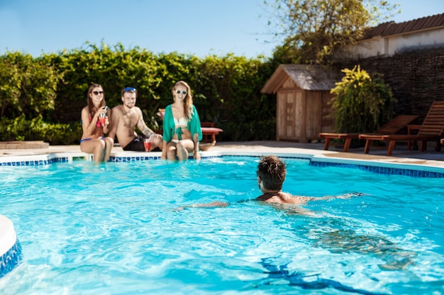 Jovens amigos alegres sorrindo, rindo, relaxando, nadando na piscina