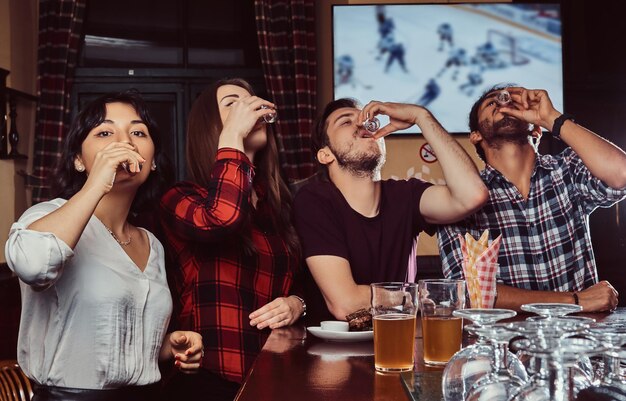 Jovens amigos multirraciais bebem vodka, descansando no pub.