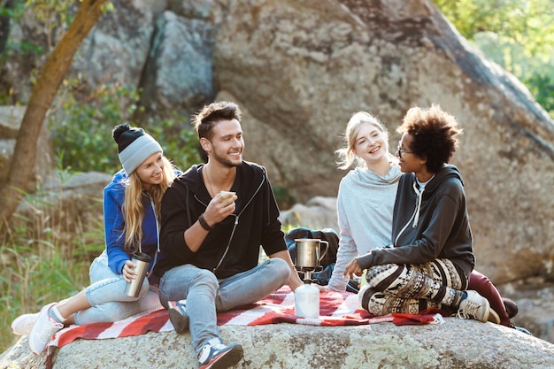 Jovens amigos sentado na pedra no canyon, sorrindo, bebendo chá