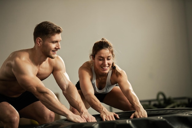 Jovens atletas sorridentes fazendo esforço enquanto se exercitam com pneu pesado em uma academia