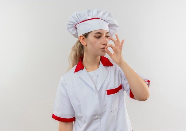 Jovens bonitas cozinheira em uniforme de chef olhando para o lado e fazendo gestos saborosos