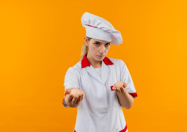 Jovens bonitas cozinheira em uniforme de chef segurando e esticando ovos