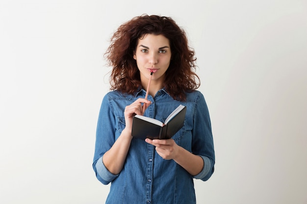 Jovens bonitas mulher segurando o caderno, lápis nos lábios, pensando, sorrindo, cabelos cacheados, pensativo, feliz, isolado