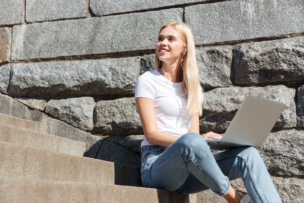 Jovens bonitas mulher sentada na escada com computador portátil