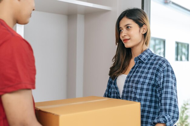 Jovens casais asiáticos ajudam a segurar uma caixa de papelão pesada a entrar em uma nova casa com felicidade, novo conceito de mudança de casa