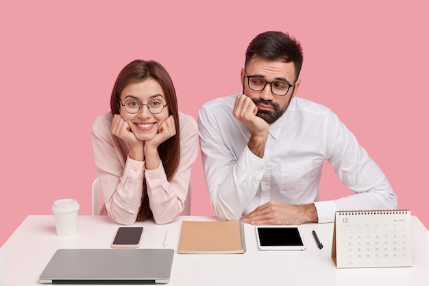 Jovens colegas de trabalho sentados à mesa com gadgets e calendário