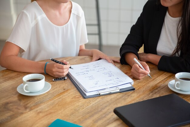 Jovens colegas femininas se reunindo e discutindo o plano de negócios, escrevendo o esquema de estratégia no papel, fazendo um rascunho