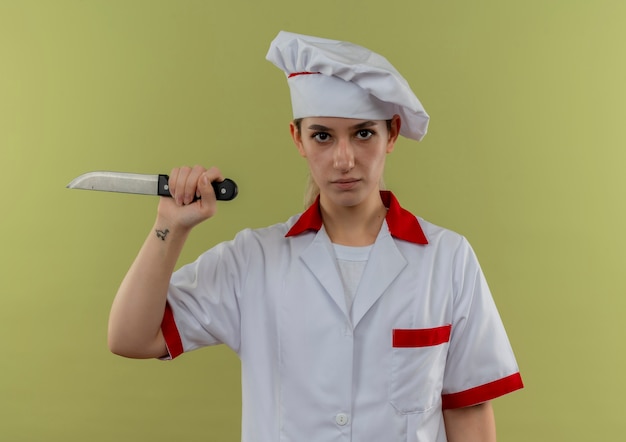 Foto grátis jovens confiantes e bonitas cozinheira em uniforme de chef segurando uma faca isolada na parede verde