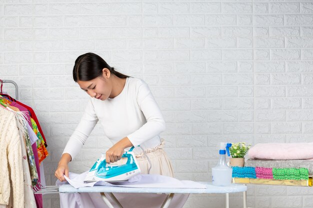 Jovens donas de casa que estão usando ferros Passando as roupas em um tijolo branco.